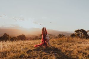 Person in flowing red dress standing on hilltop during golden hour.