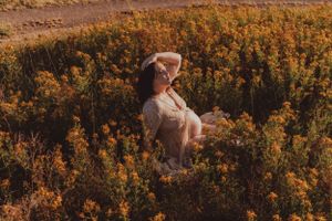 Figure in white dress sitting among golden wildflowers during sunset.