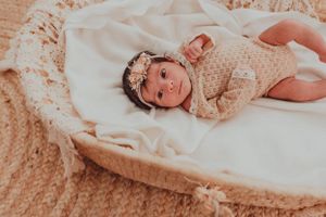 Newborn baby wearing lace outfit lying on textured cream blanket.