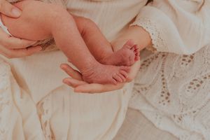 Tiny newborn baby feet resting in hands against white lace fabric backdrop.