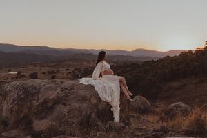 A figure in white stands among rocky desert terrain at sunset with mountains in the distance.