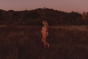 A silhouette walks through a golden field at sunset with trees in background.