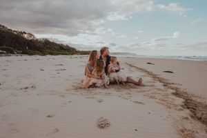 Couple sitting on a sandy beach with a golden retriever dog, enjoying a relaxed outdoor moment.