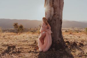 Ethereal pink dress photographed against tree trunk in sunset mountain landscape.