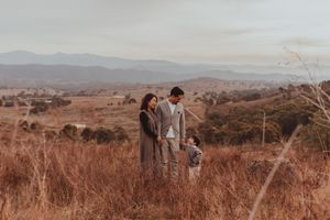 A couple stands together on a hilltop overlooking mountains and valleys in warm autumn colors at sunset.