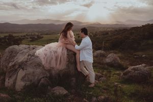 Couple sharing a tender moment on rocks at sunset with scenic mountain valley views during maternity photo shoot.