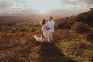 Couple embracing at golden sunset on a scenic hilltop with rolling green valleys and mountains in background.