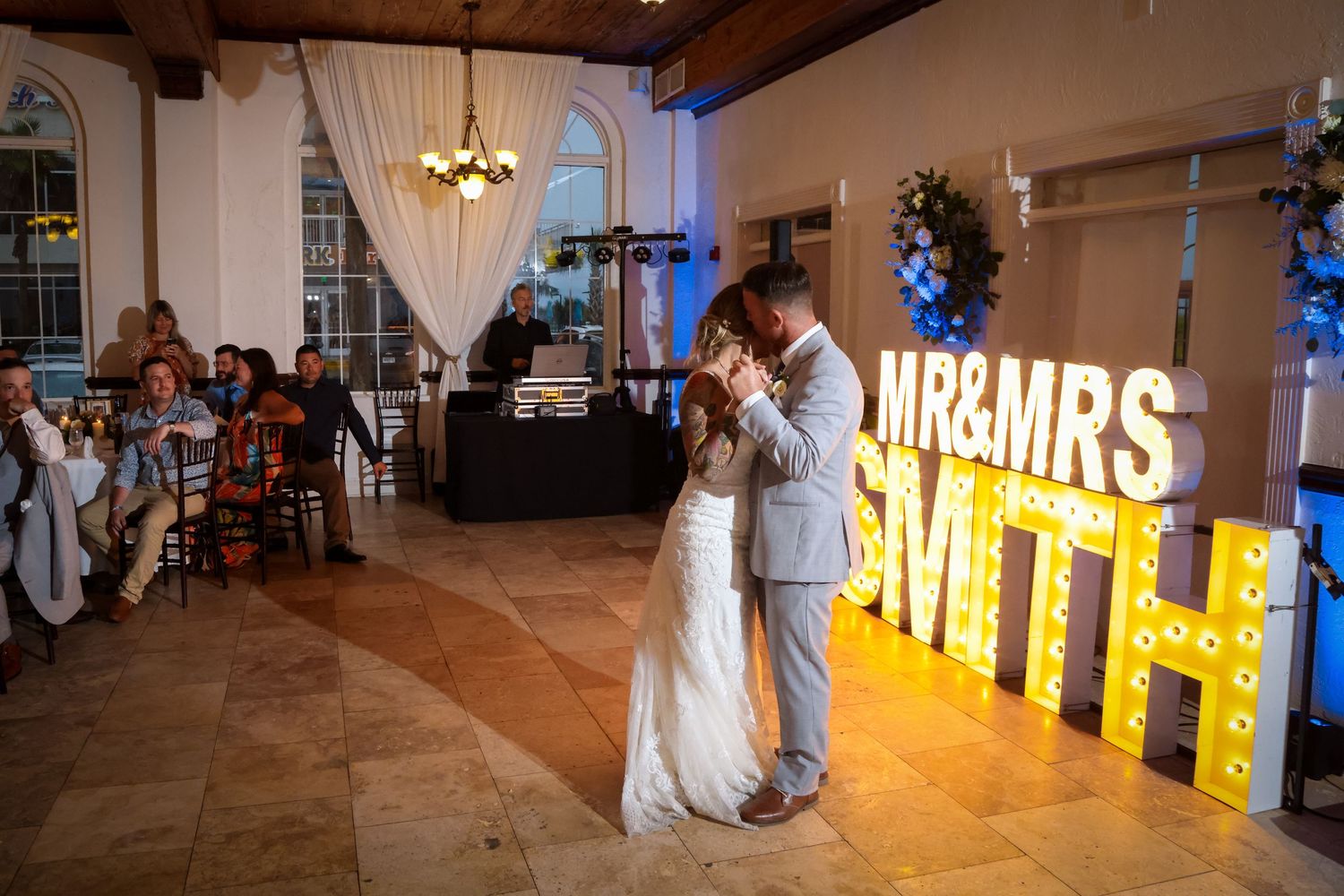 Wedding couple shares their first dance in front of illuminated marquee letters spelling MR&MRS SMITH.