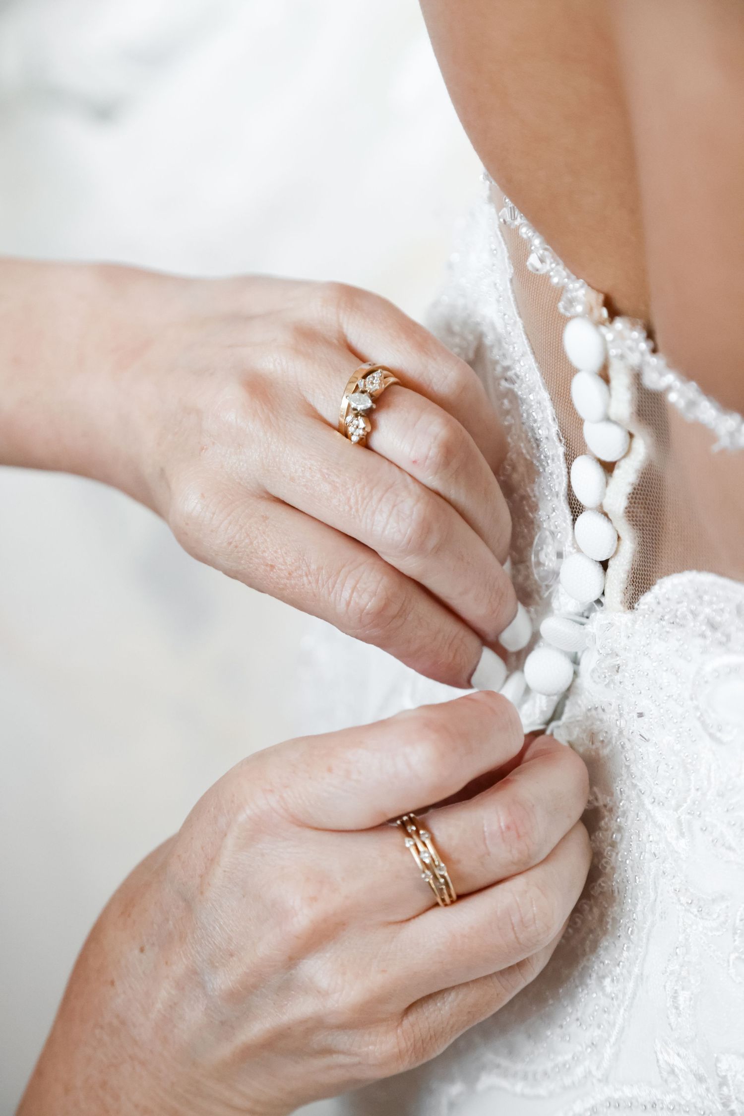 Detail shot of hands with wedding rings adjusting delicate lace on a wedding dress.