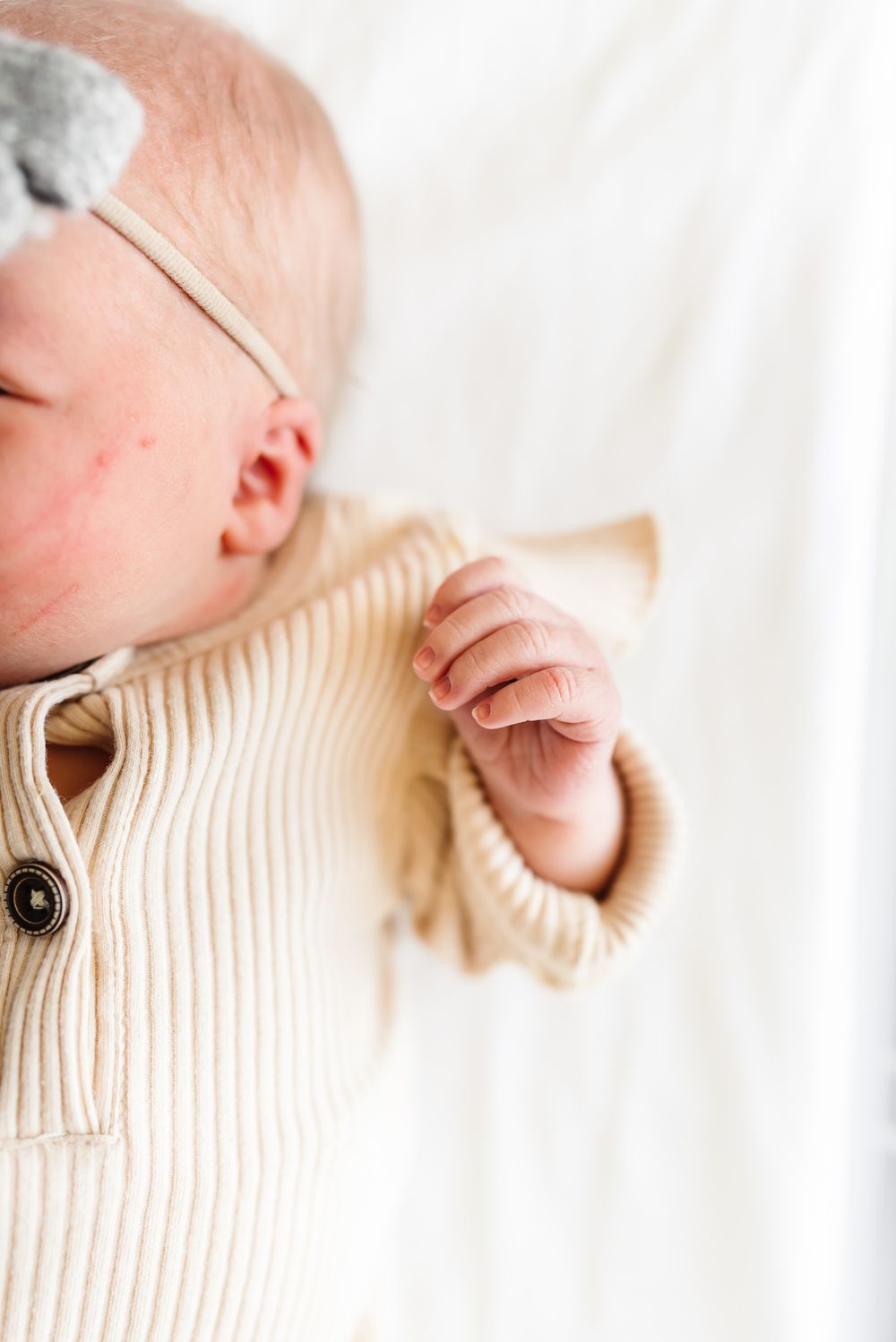 Newborn wearing cream colored ribbed sweater on white blanket.