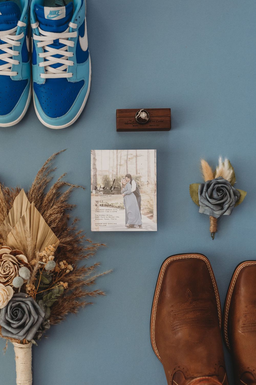Wedding details flat lay with blue sneakers, dried flowers, and brown boots against a blue background.