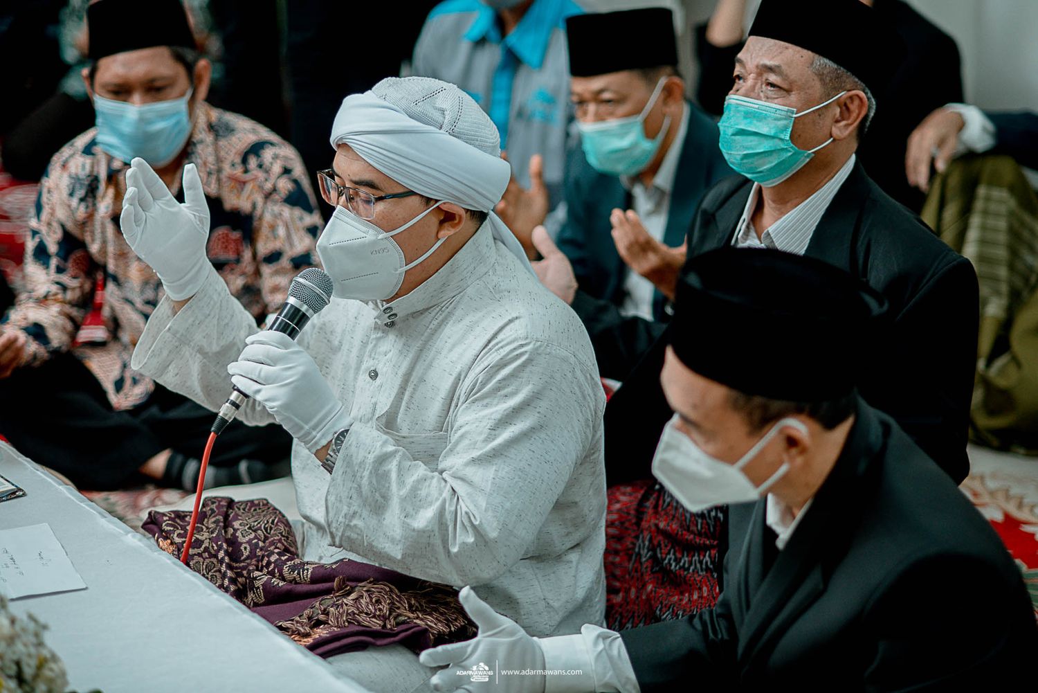 Religious ceremony participants in masks and traditional attire seated at ceremonial table.