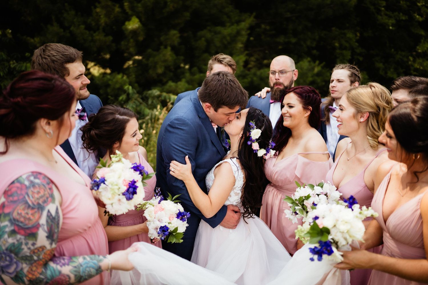 Wedding party celebrates joyfully together with pink dresses and flower bouquets at outdoor ceremony.