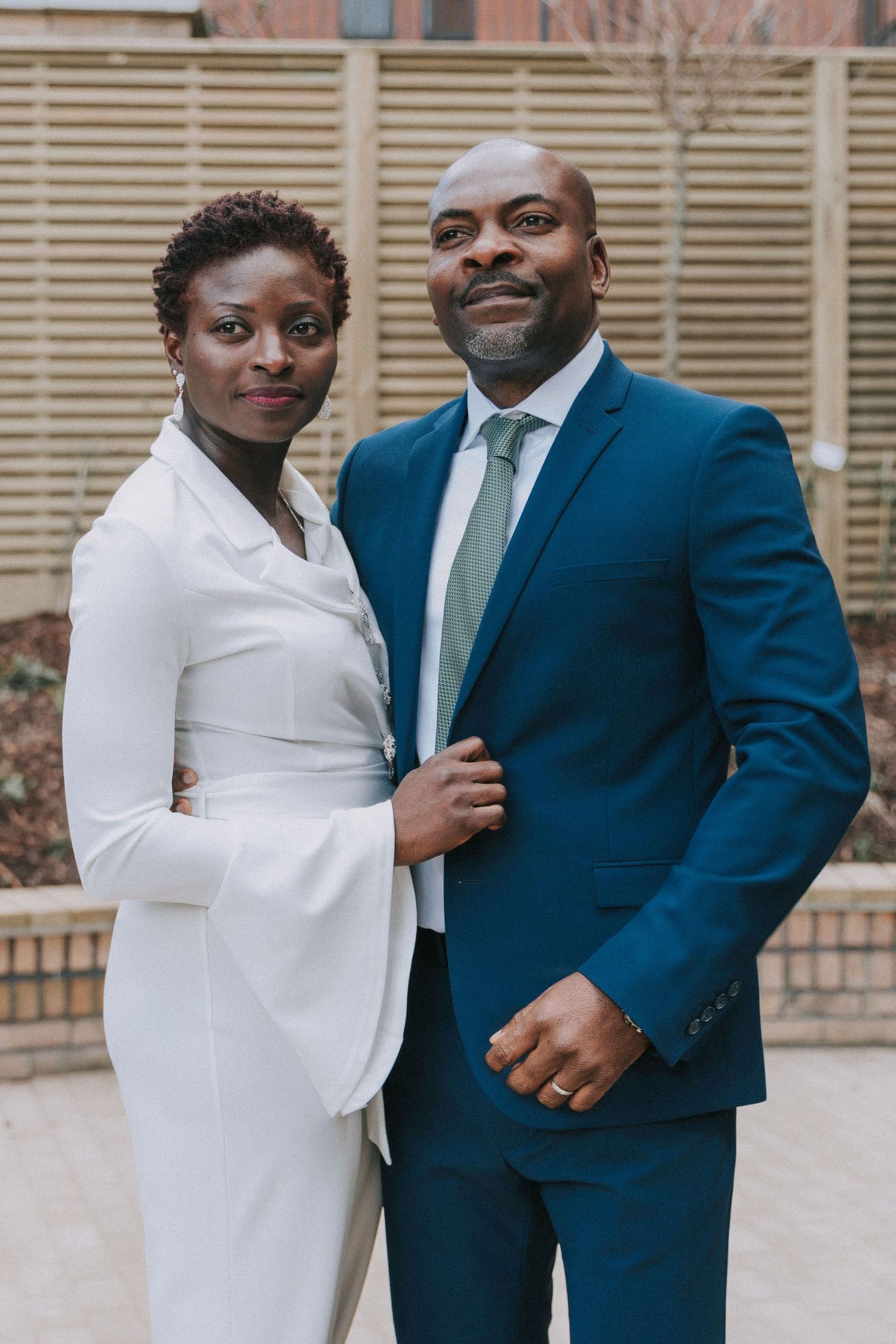 A couple poses together outside in formal wedding attire.