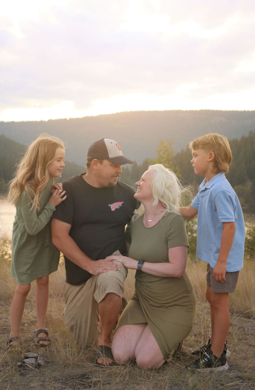 Candid family moment captured on hillside during golden hour with mountain backdrop.