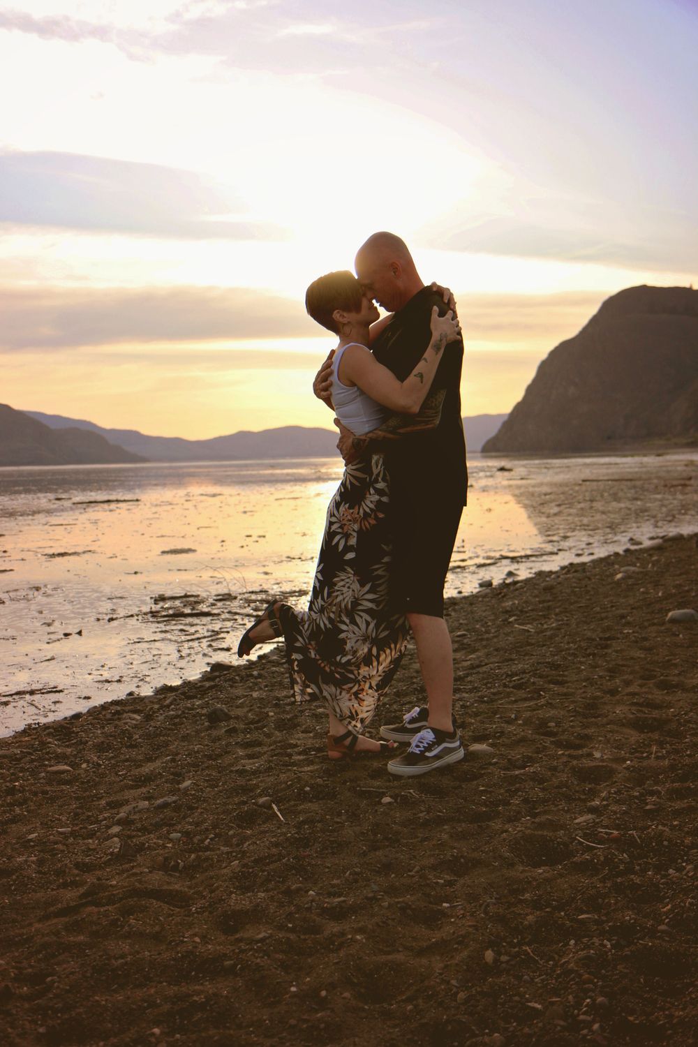 A romantic couple moment captured against a sunset beach backdrop with mountains.
