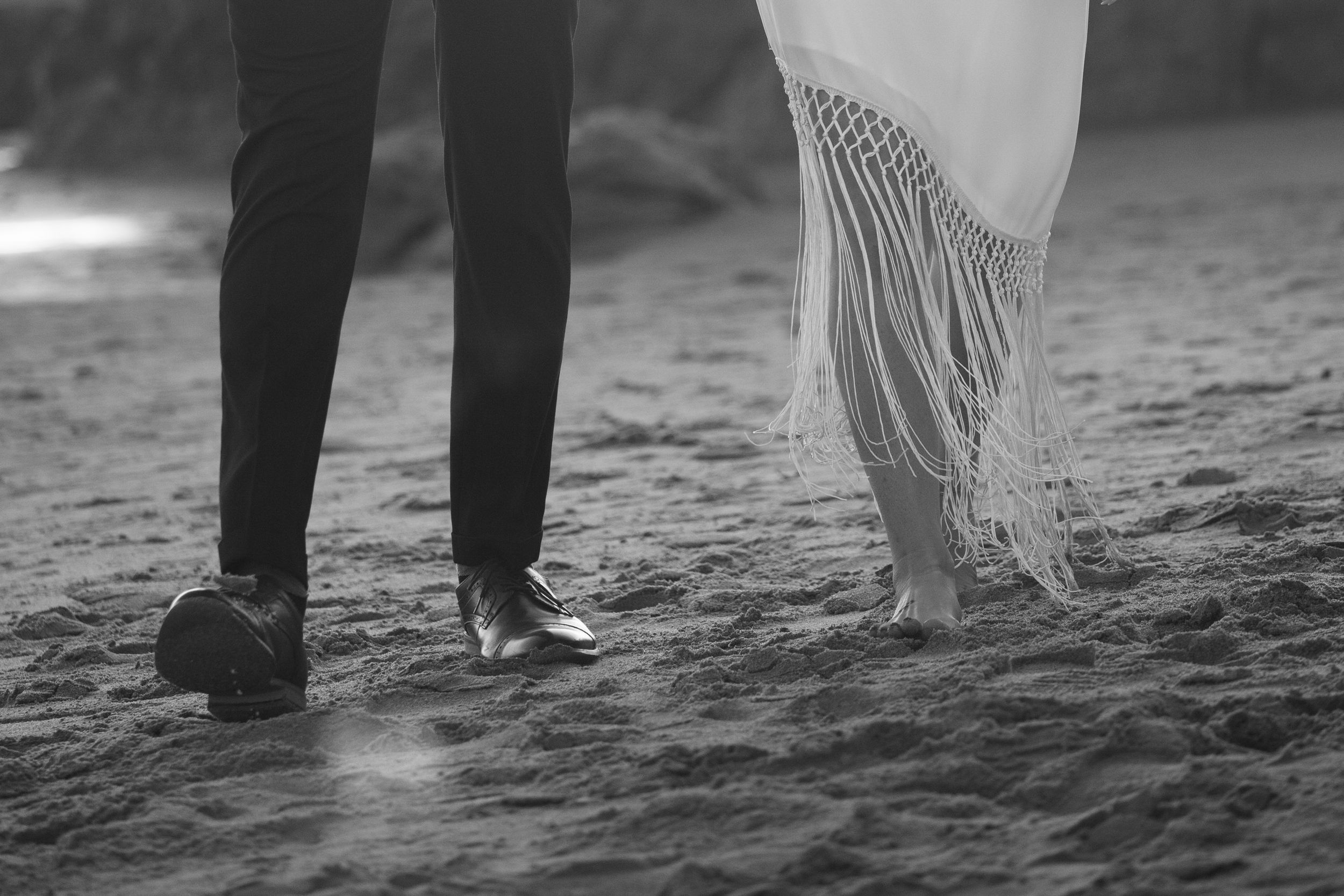 Black and white photo of two pairs of feet standing on sandy beach.