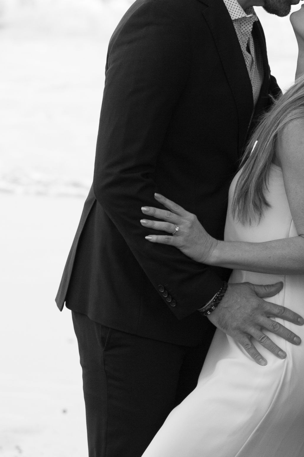 Close-up black and white photo showing couple embracing, with focus on formal attire and ring.