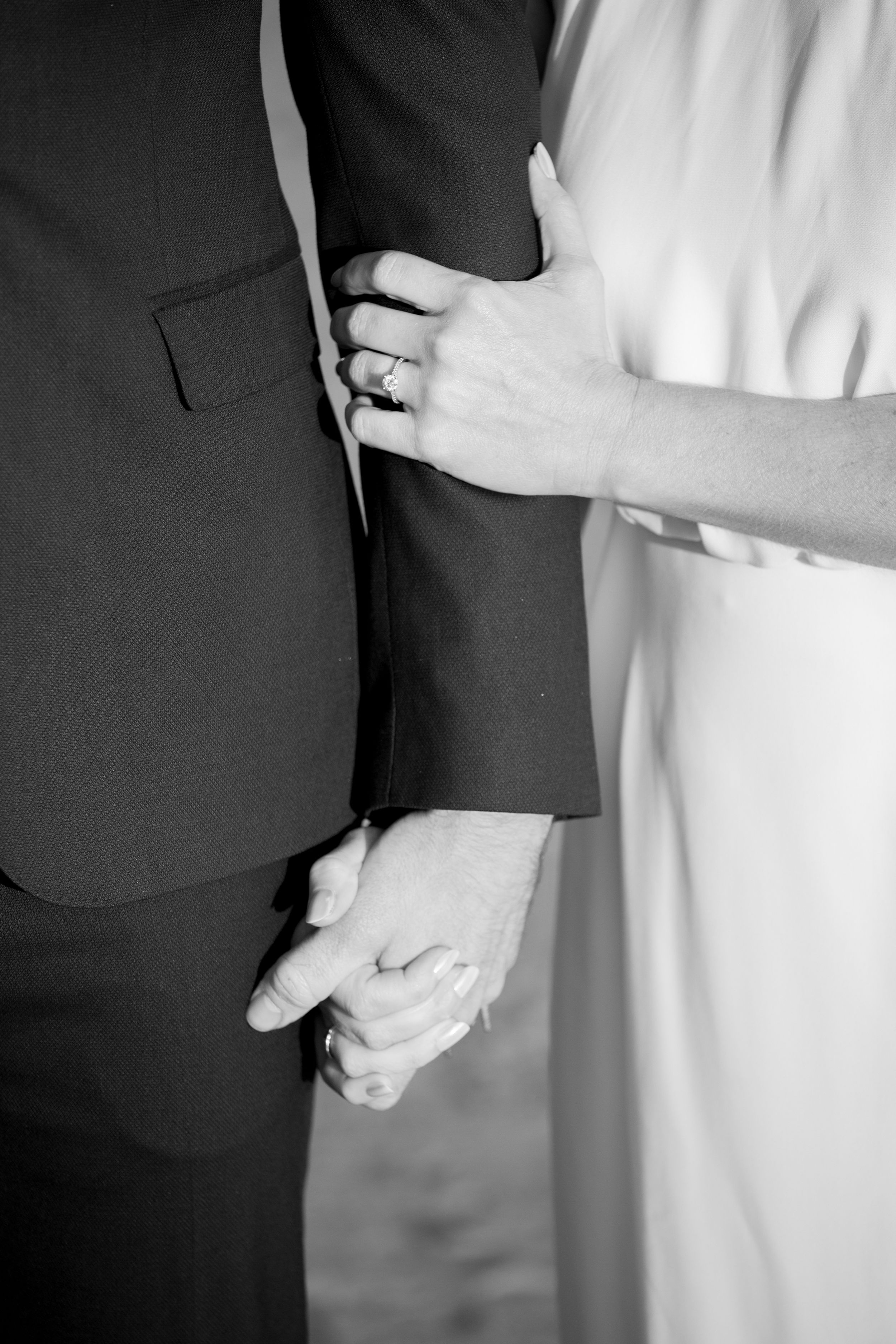 Black and white detail shot of couple holding hands showing wedding rings.