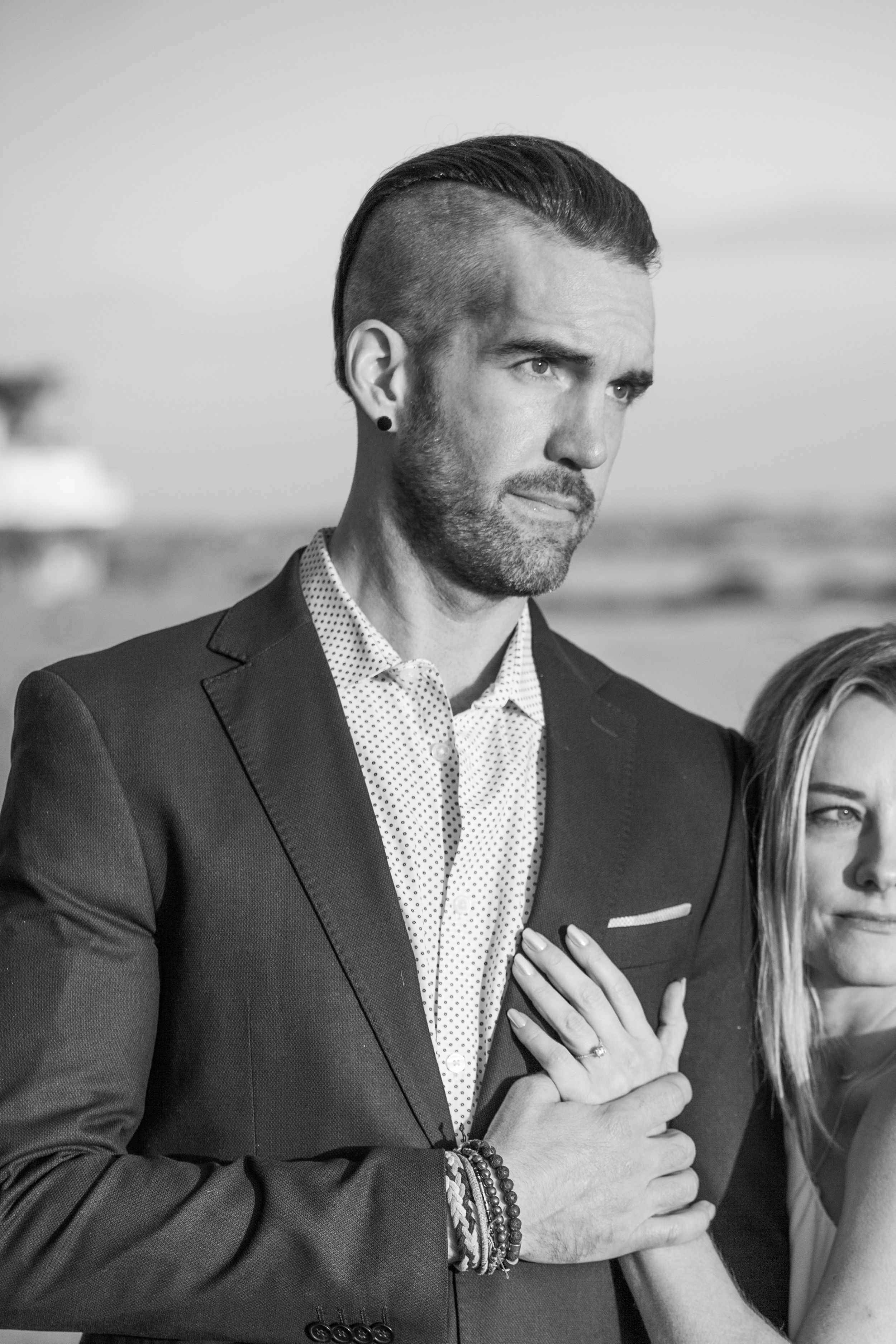 Black and white portrait of couple in formal attire against coastal backdrop.