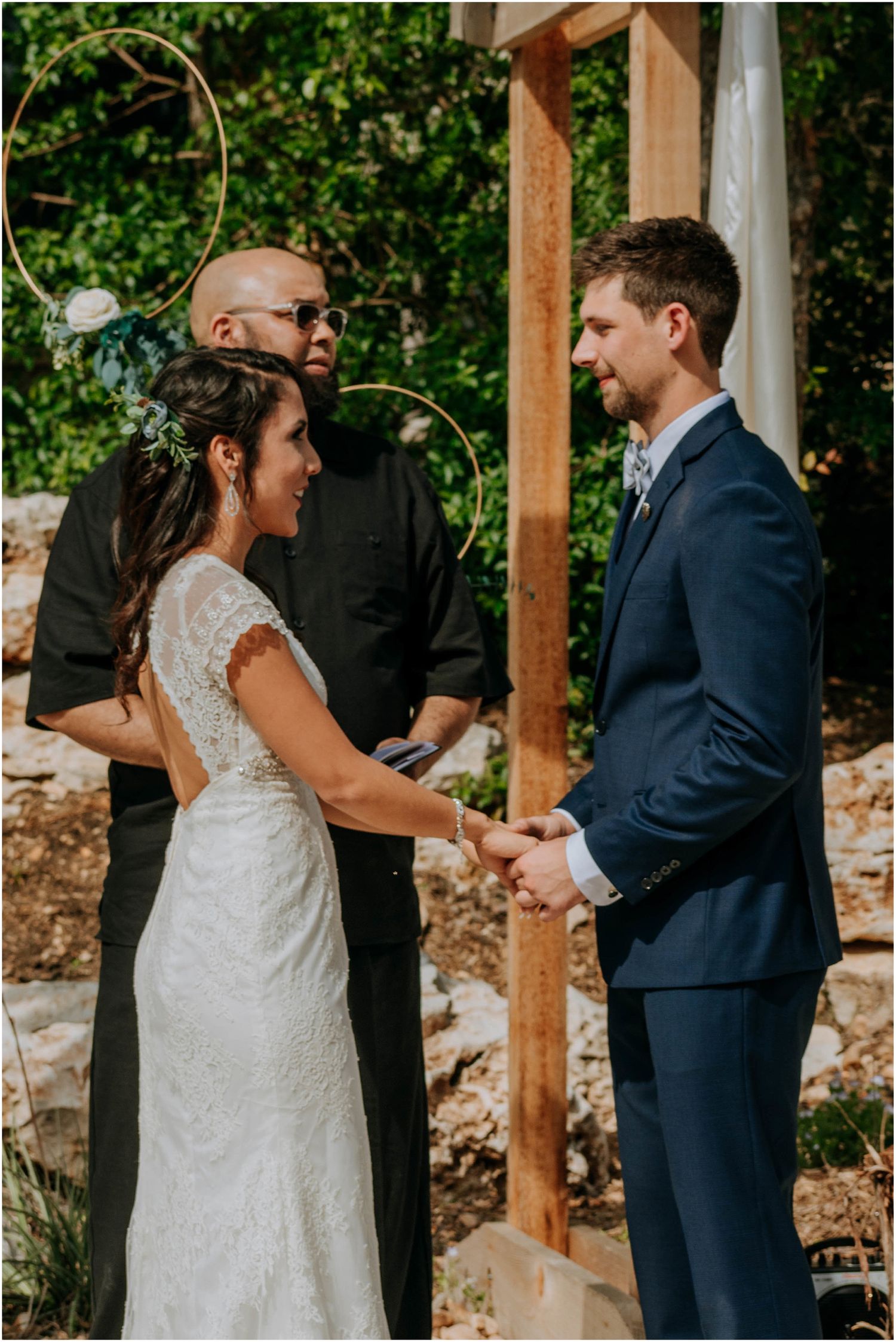 An intimate outdoor wedding ceremony taking place under a wooden arch with natural surroundings.