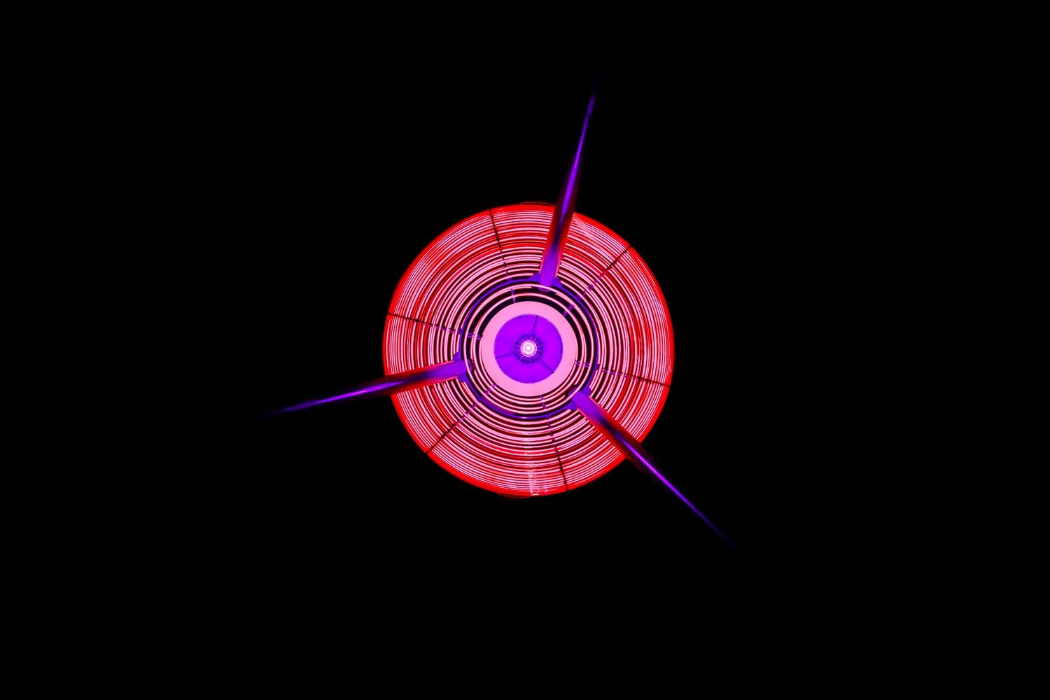 A circular red and purple neon light pattern creates a geometric design against black background.