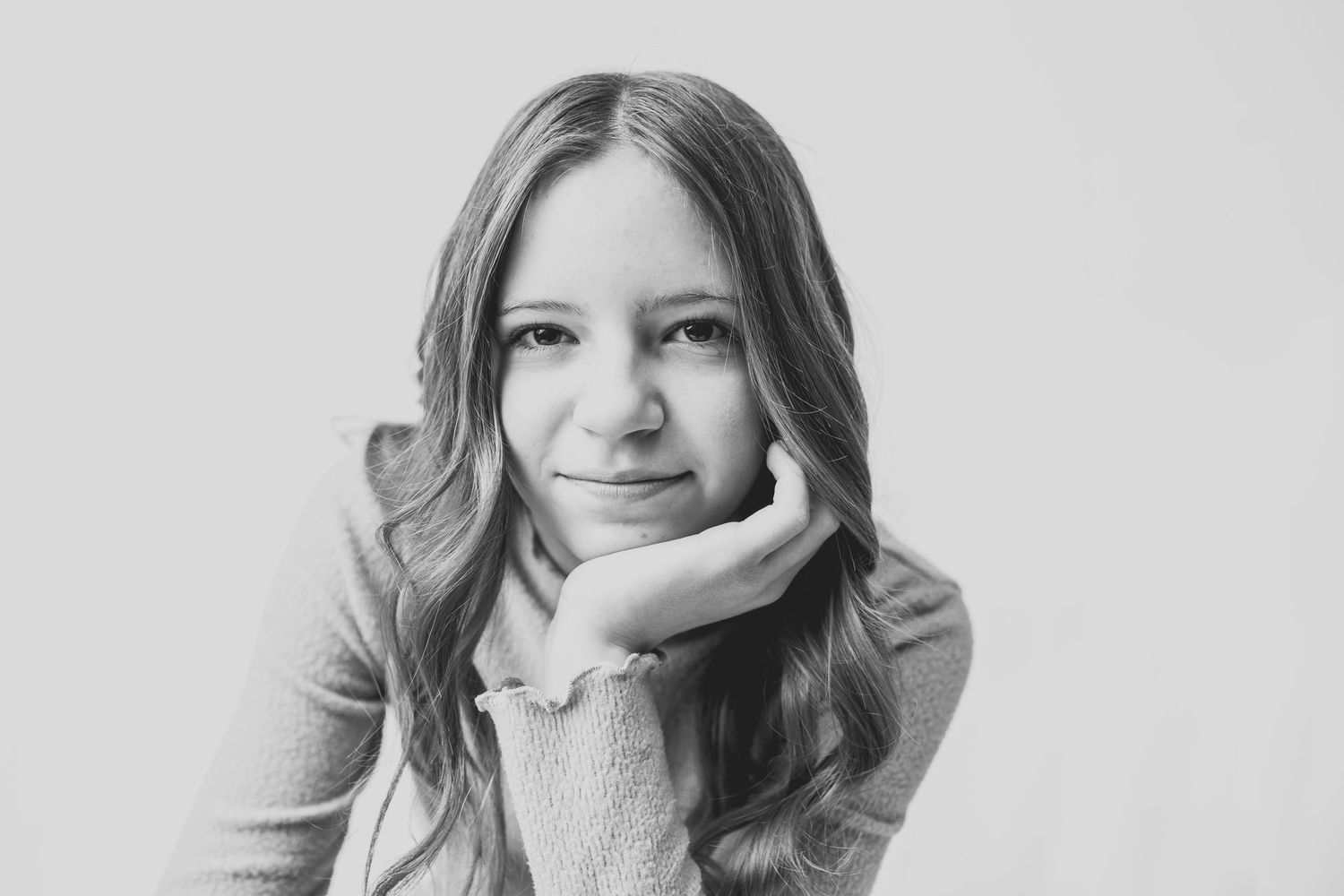 Black and white headshot of someone with wavy hair resting their chin on their hand.
