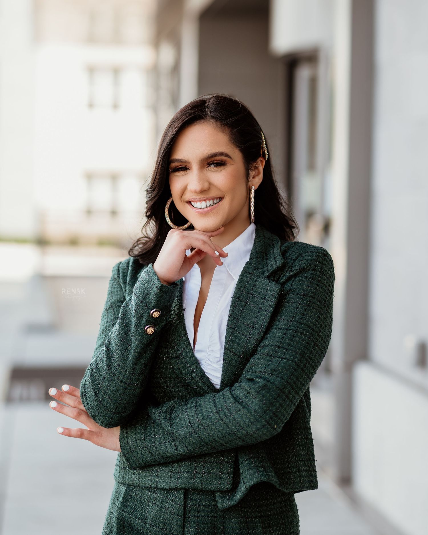 Professional portrait of someone in a dark green business suit against a light building exterior.