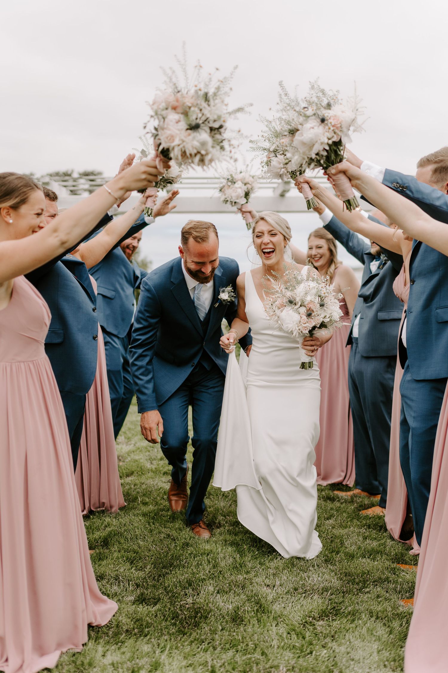 Candid wedding party photo with everyone laughing together on grass.