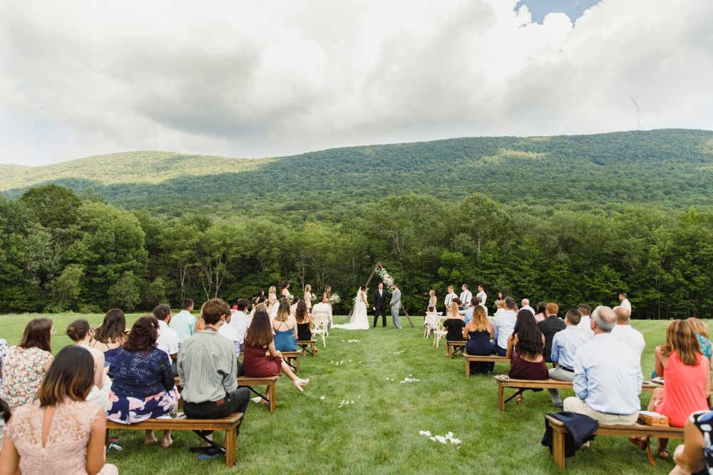Panoramic view of wedding guests seated on wooden benches overlooking mountain landscape.