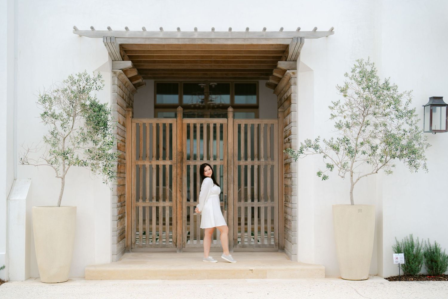 Person in white dress standing before wooden slatted doors with modern architectural details.