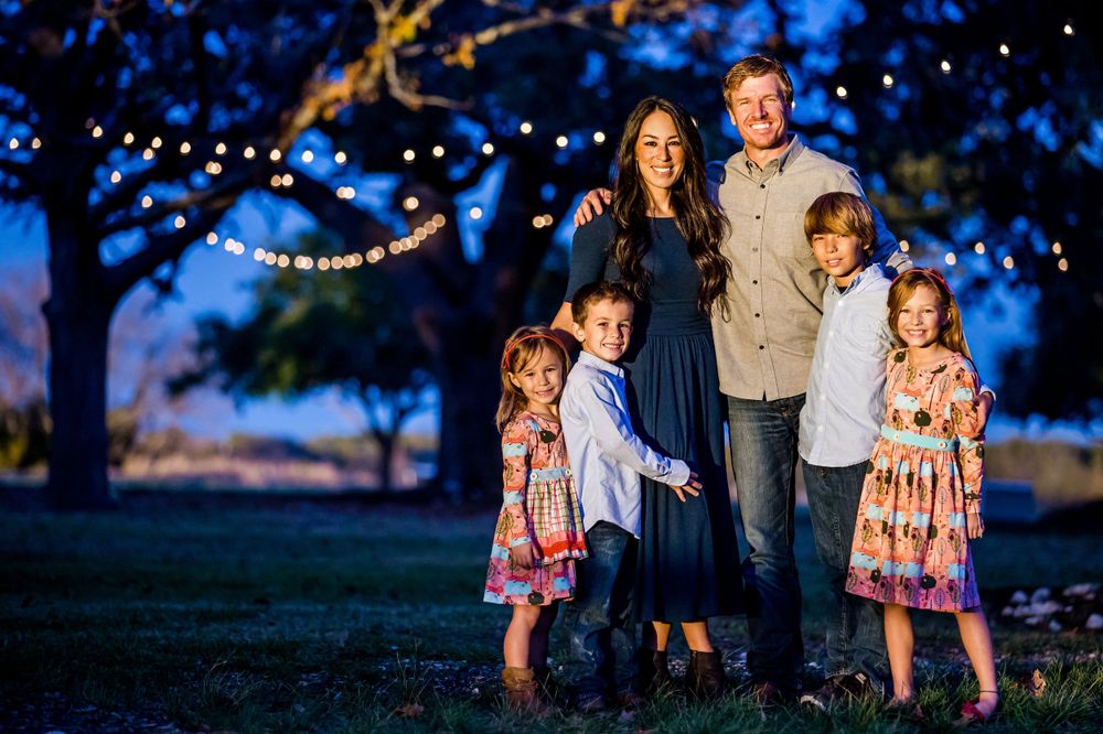 Family portrait at twilight with string lights glowing in trees behind them.