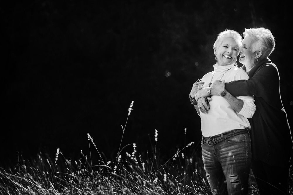 Intimate black and white portrait of two people embracing in tall grass at night.