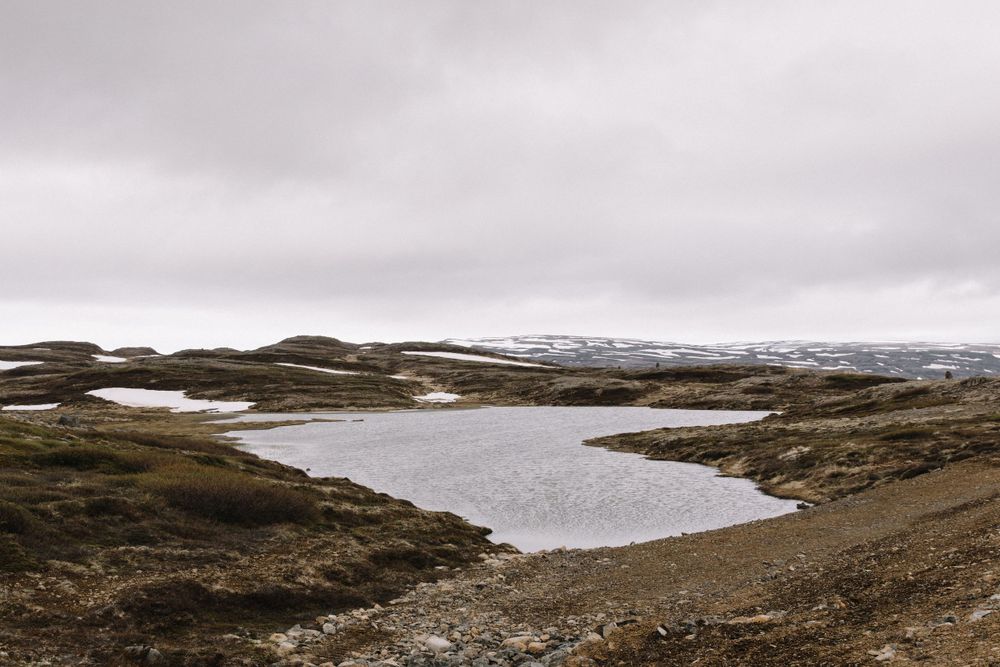 A barren highland landscape with small lakes and snow patches under cloudy skies.