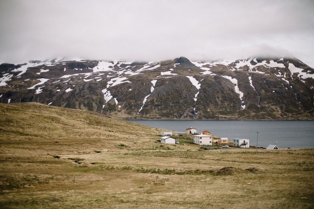 Remote coastal settlement with buildings along a fjord surrounded by snow-capped mountains.