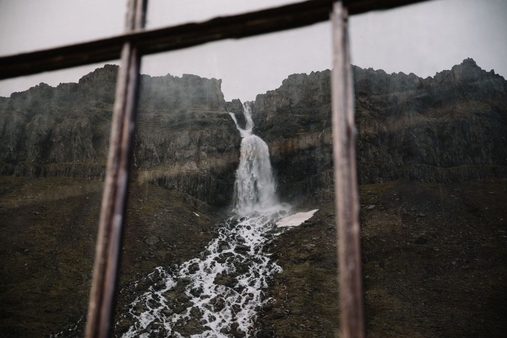 Dramatic waterfall cascading down rocky cliff viewed through window frame.