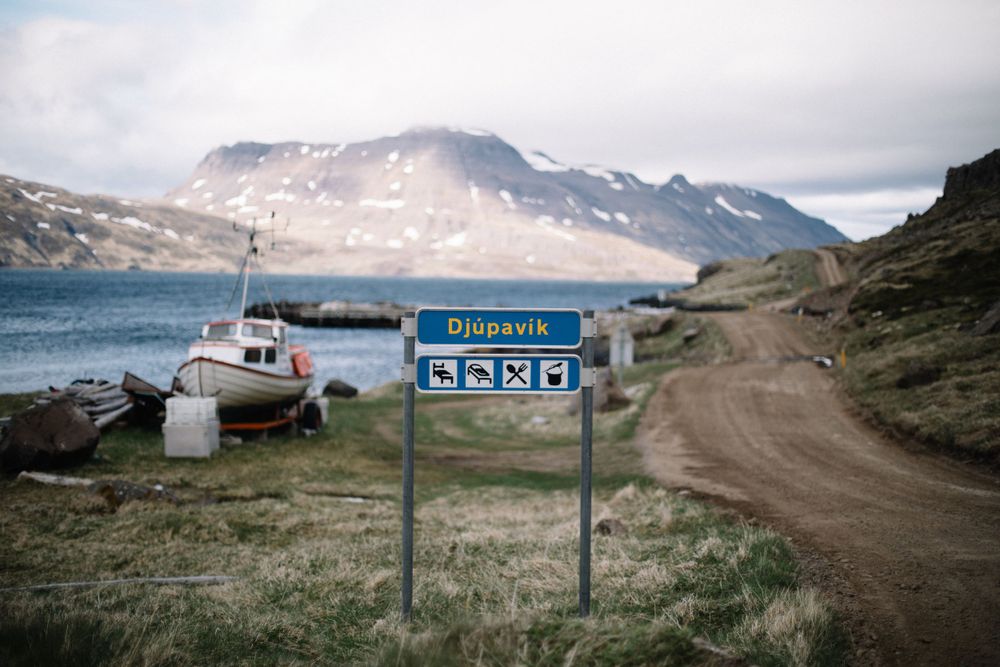 Directional sign with boat in background along coastal road in remote Nordic landscape.