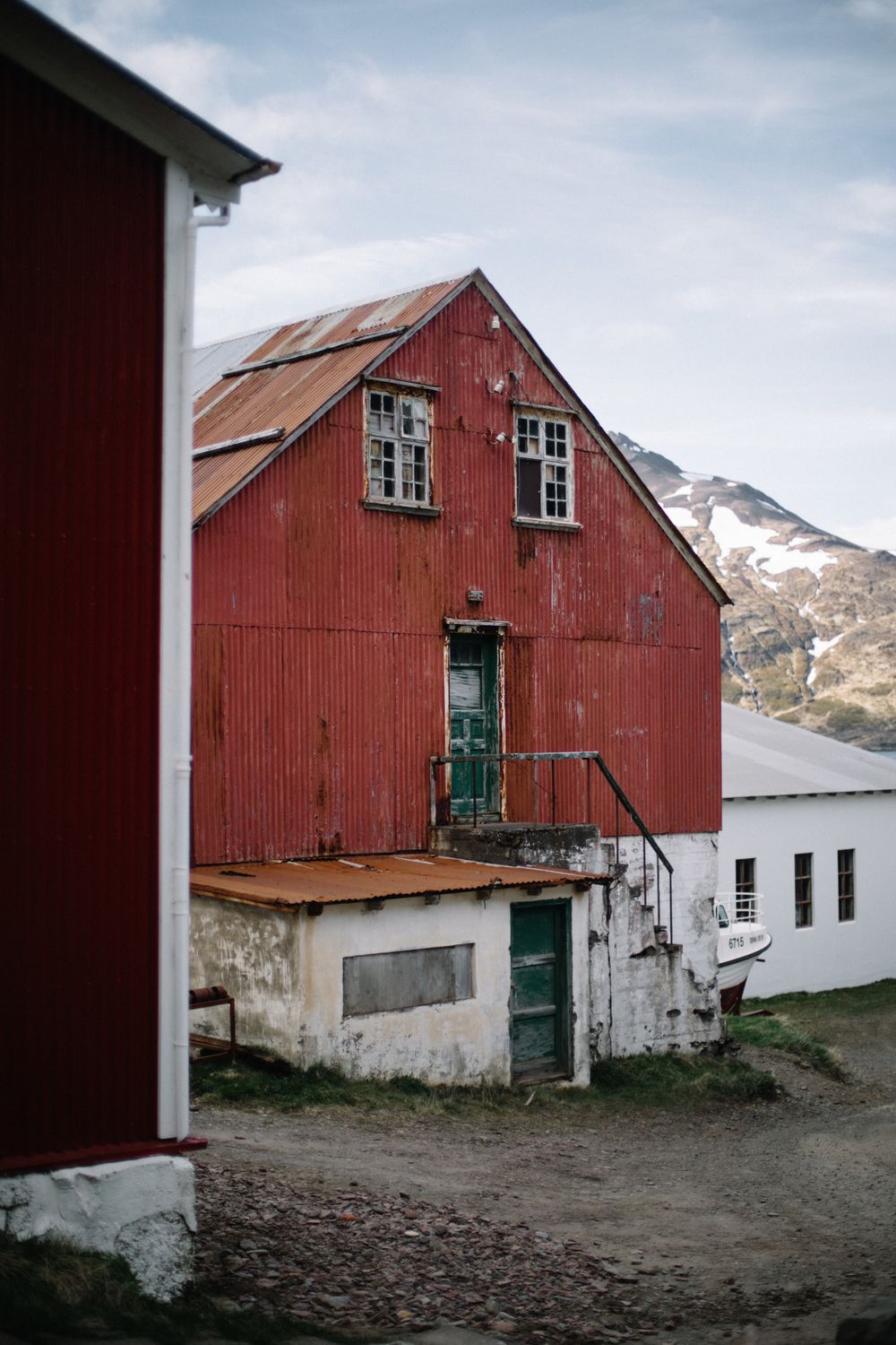 Weathered red barn building with white foundation against mountainous backdrop.