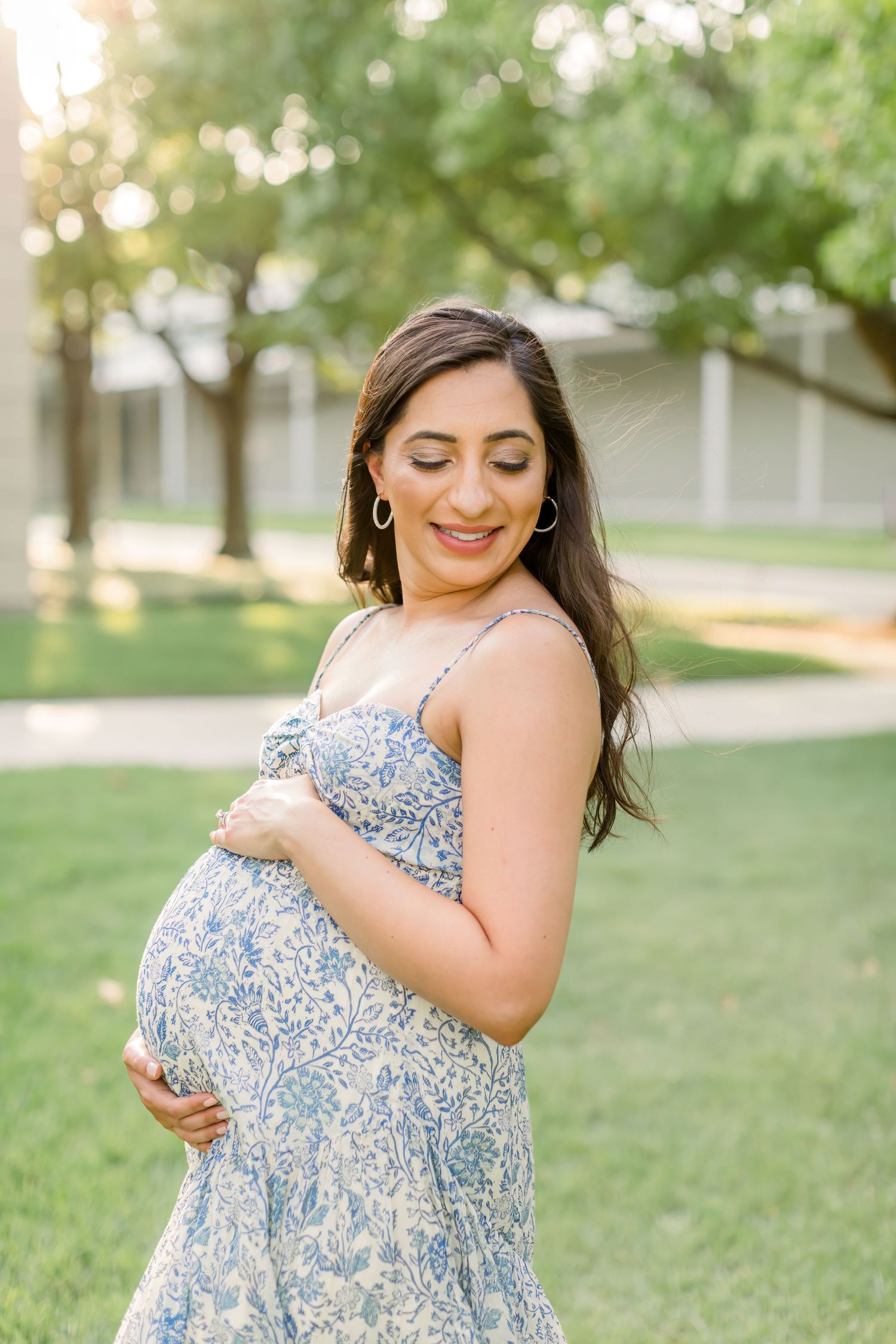 Pregnant woman in blue floral dress smiles while holding her baby bump.