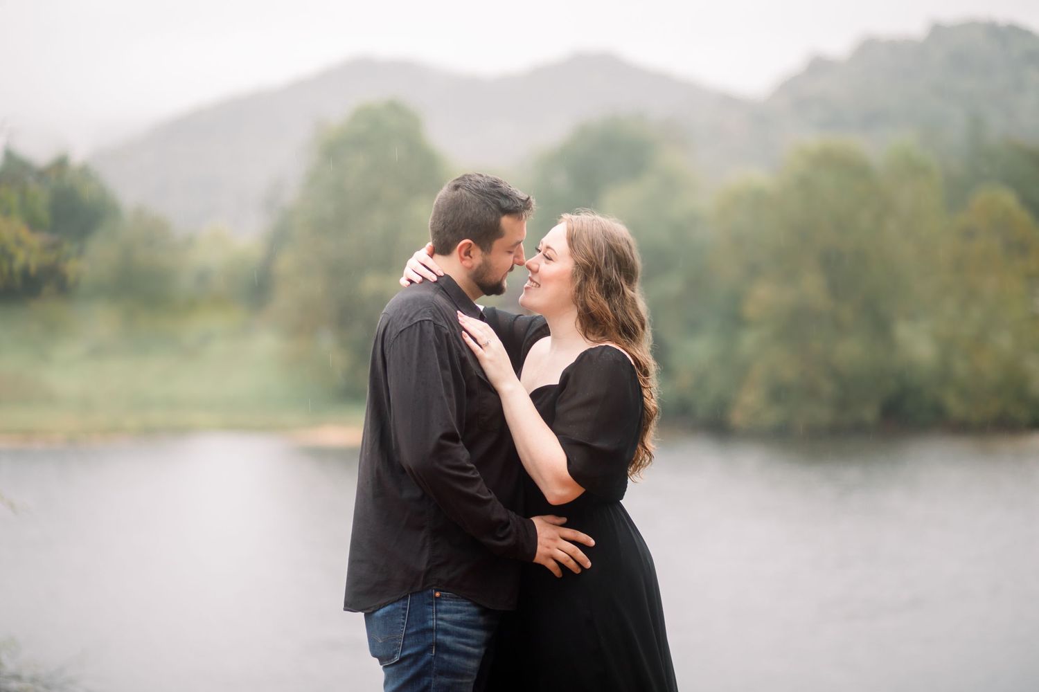 A romantic couple shares an intimate moment by a misty lake during an outdoor photoshoot.