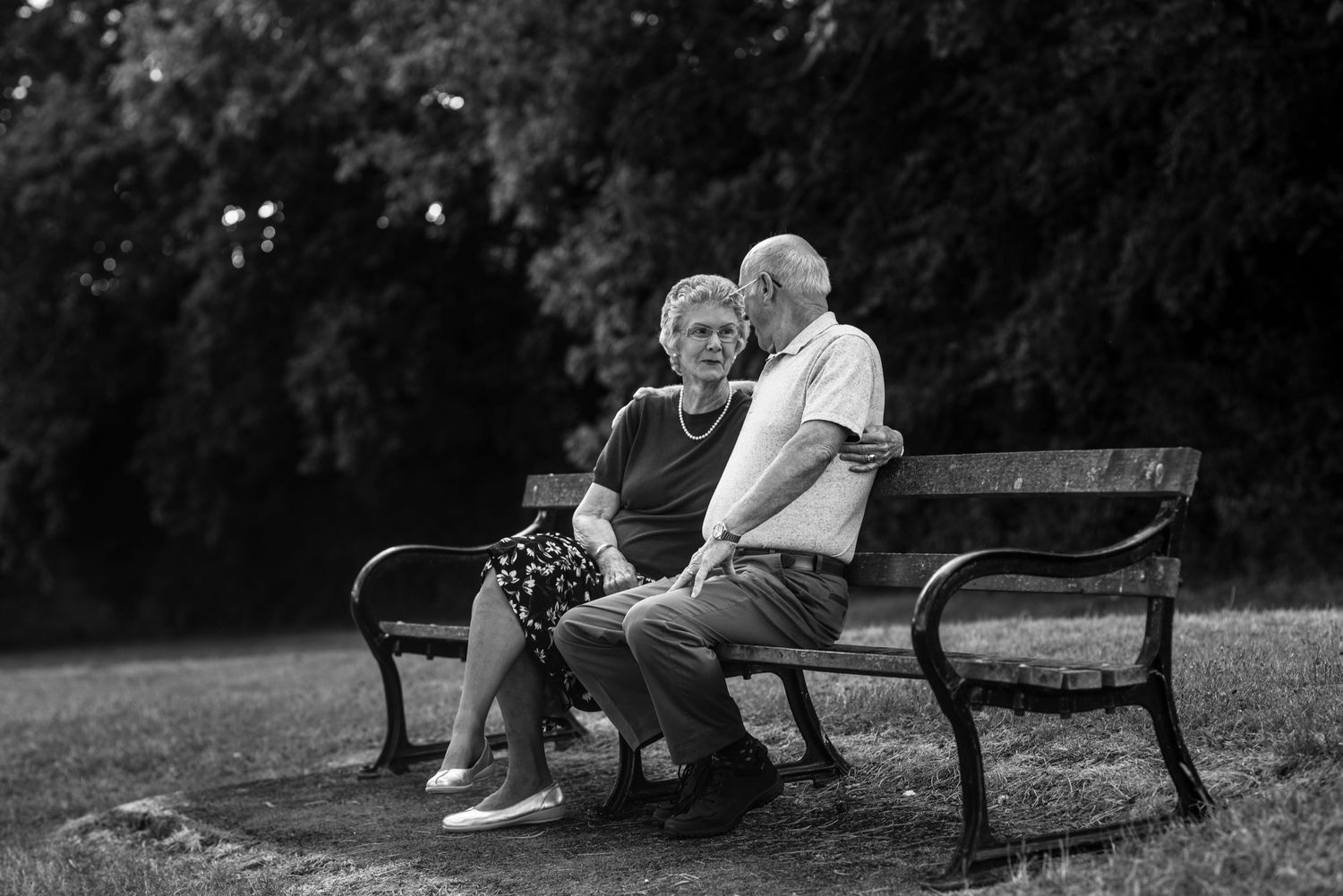 Black and white photo of couple relaxing on park benches.