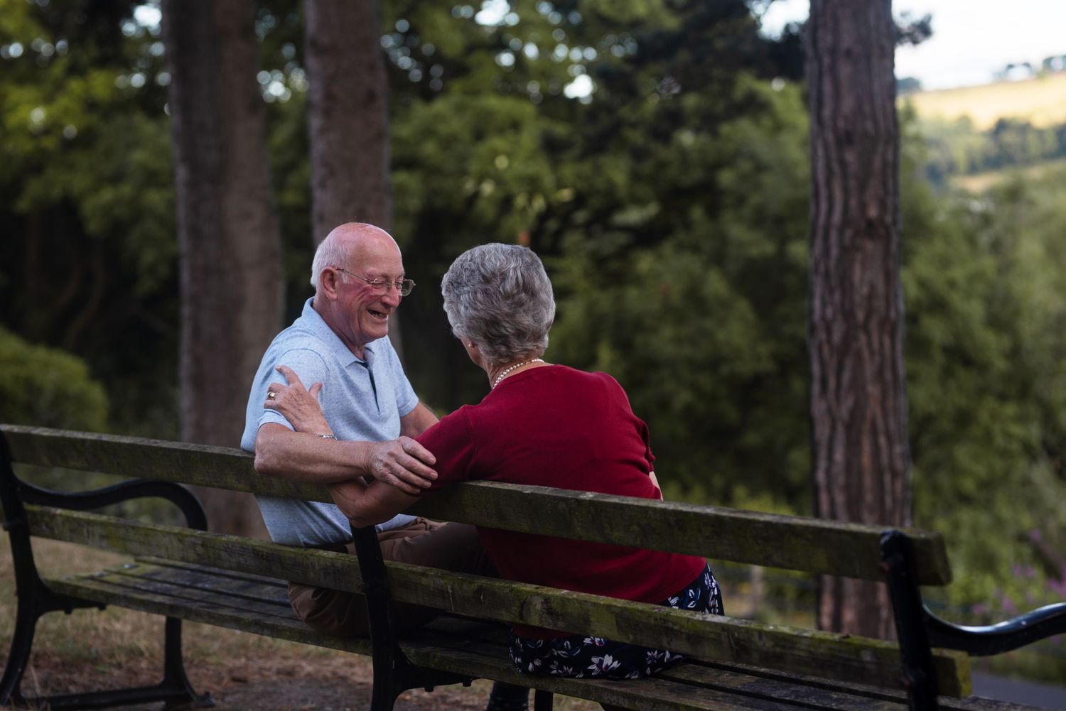 Elderly couple sharing a tender moment on a wooden bench in a peaceful forest setting.
