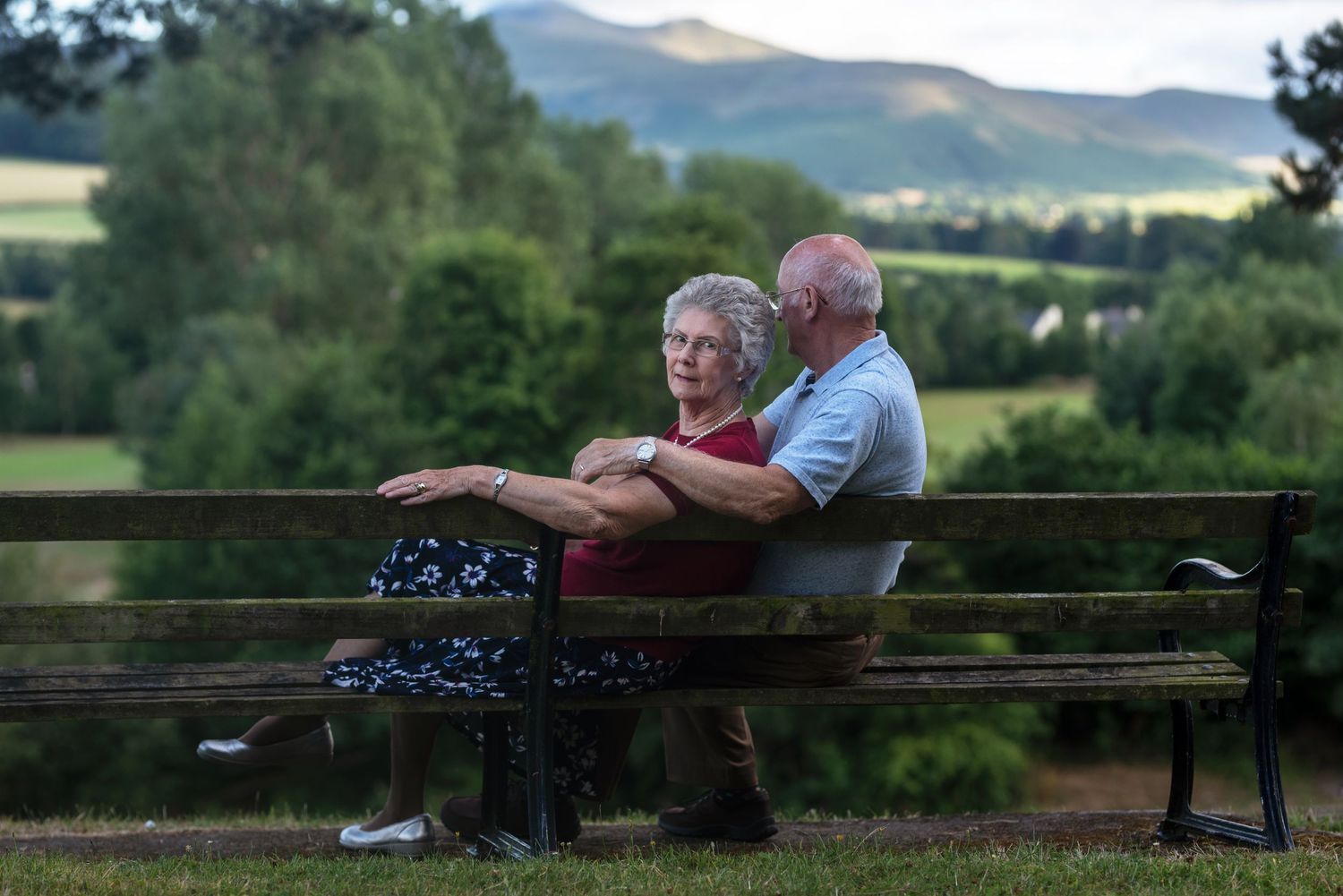 Couple enjoying a quiet moment on a bench with scenic countryside views.