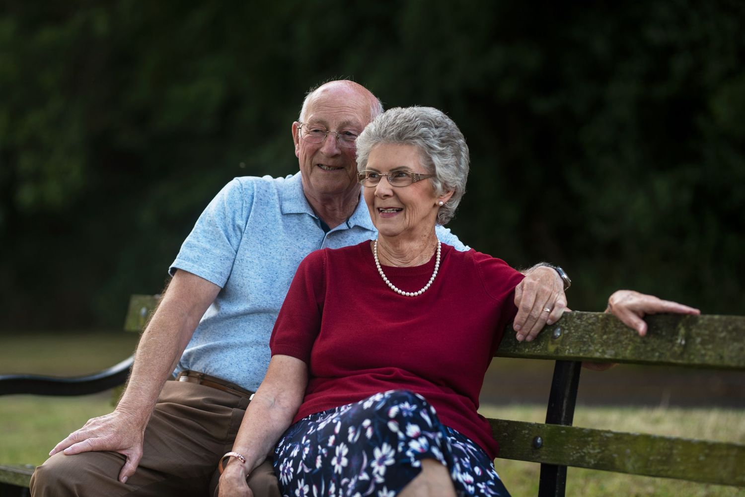 A couple sitting together on a park bench during sunset.
