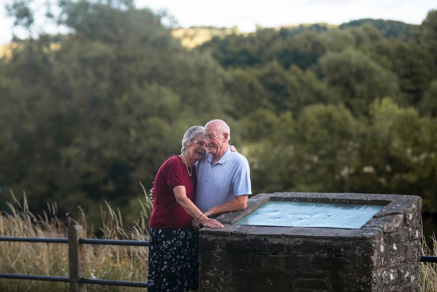 Couple sharing an intimate moment on a wooden bench overlooking a scenic mountain landscape at sunset.