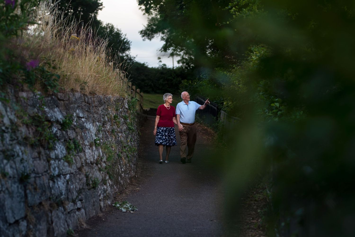 Walking path along stone wall with greenery in late afternoon light.
