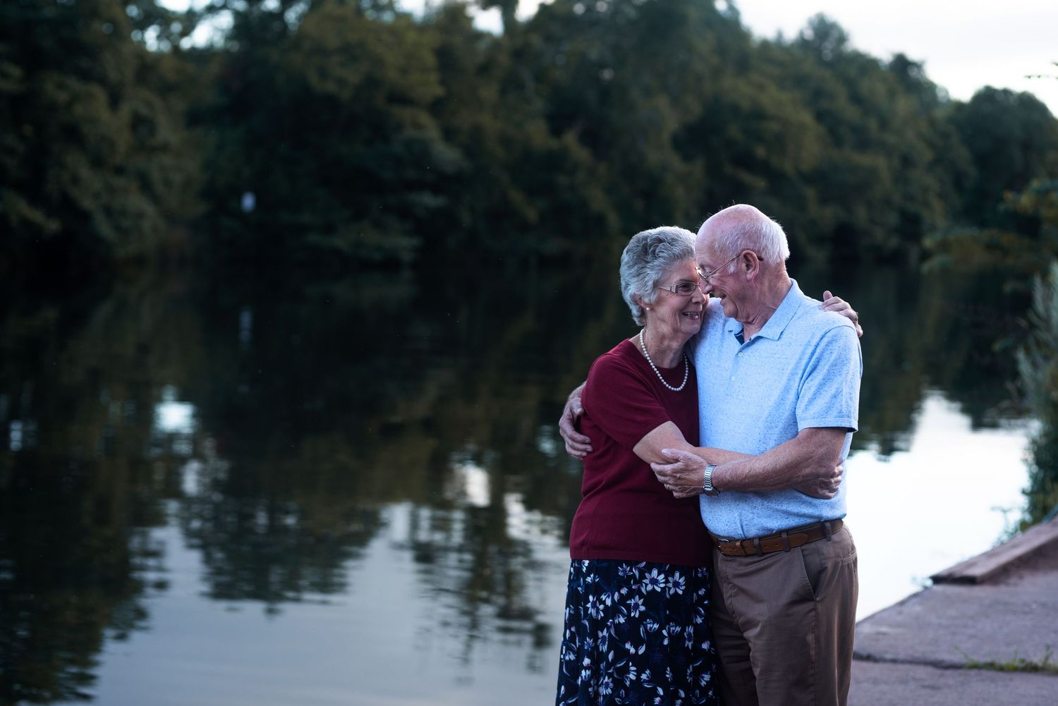Couple sitting close together on a bench near a serene lake during golden hour.