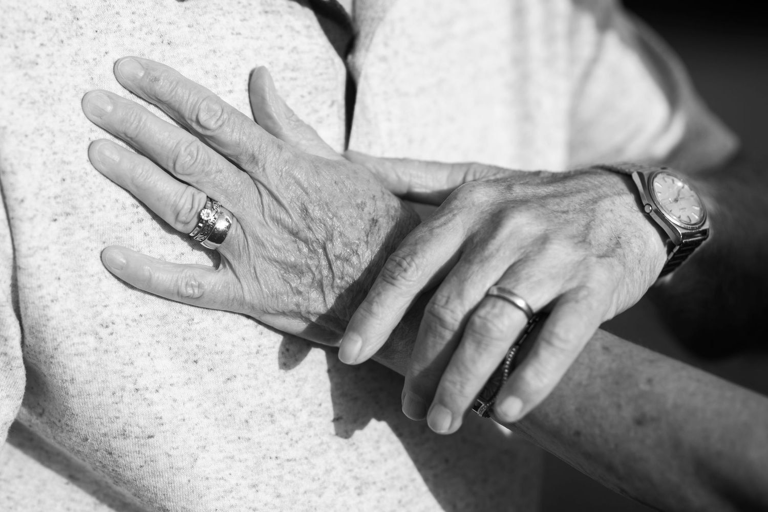 Close-up shot of hands wearing wedding rings against a black background.