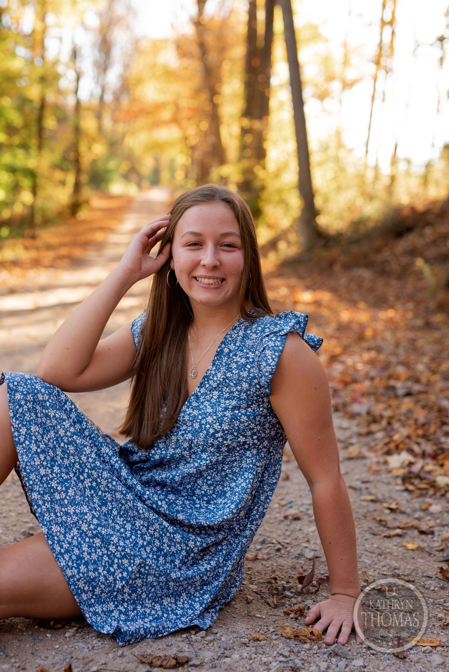 An autumn photoshoot featuring a blue floral dress against a backdrop of fallen leaves.