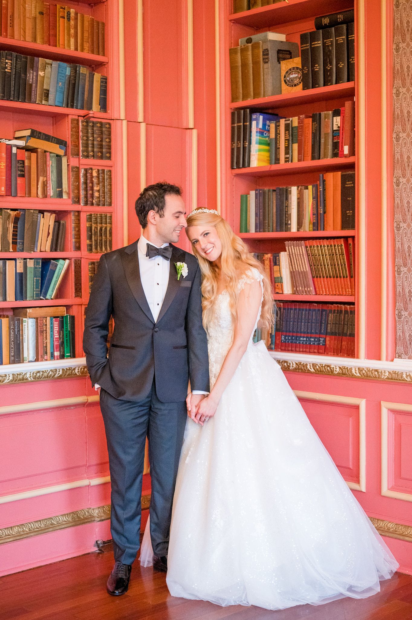 Bride smiling at the camera while resting her head on the groom's shoulder in the NYIT library.